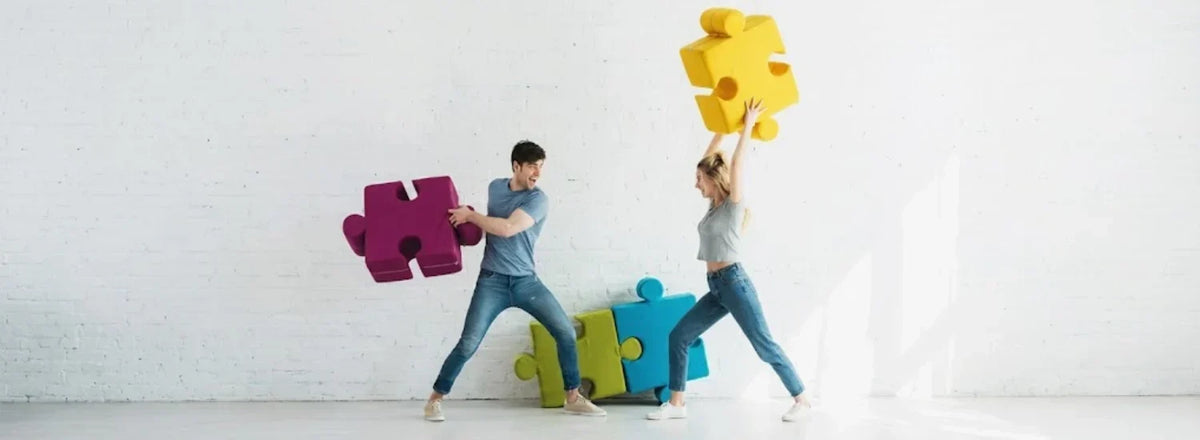 A couple playfully fighting one another with giant foam jigsaw puzzle pieces.