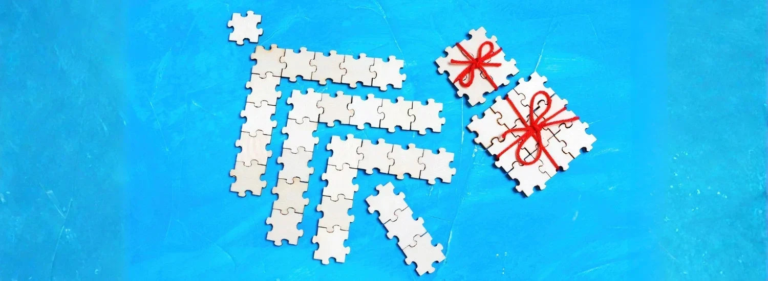White jigsaw puzzle pieces artfully lain out to form the shape of a Christmas tree and two wrapped presents.