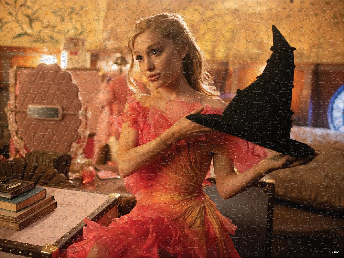 A scene from the movie Wicked, with Glynda in a pink dress holding up Glynda’s pitch-black witch’s hat. The picture is stylized with an overlay of jigsaw puzzle piece outlines.