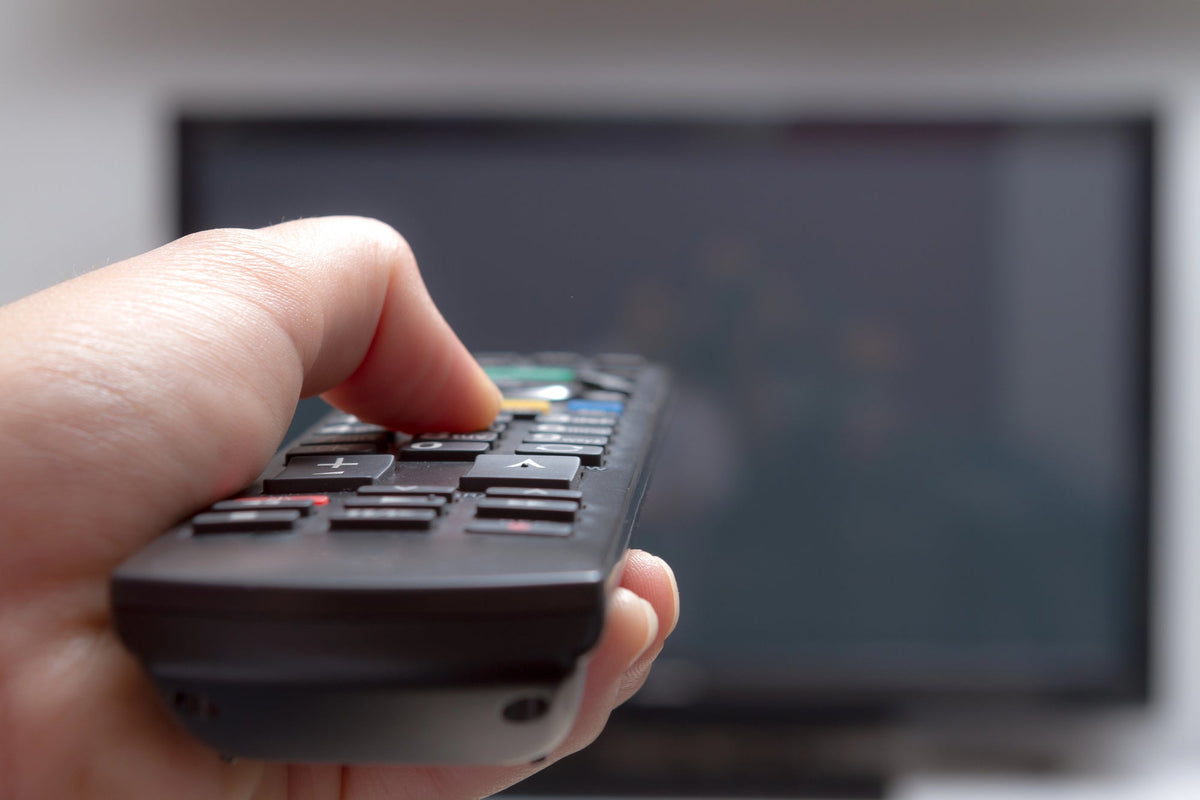 A photo of a hand holding a TV remote up to a television on the wall.