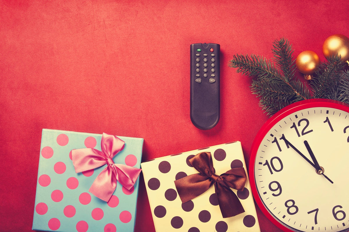 Several wrapped presents, a tv remote, a clock, and a Christmas tree branch laying together on a red background.