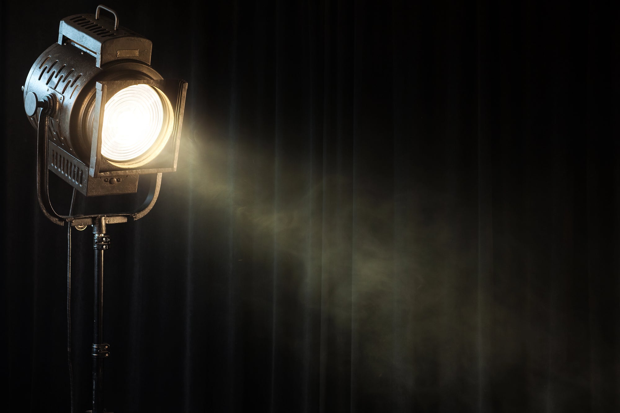 A theatre spotlight shining on a black curtain in the dark.