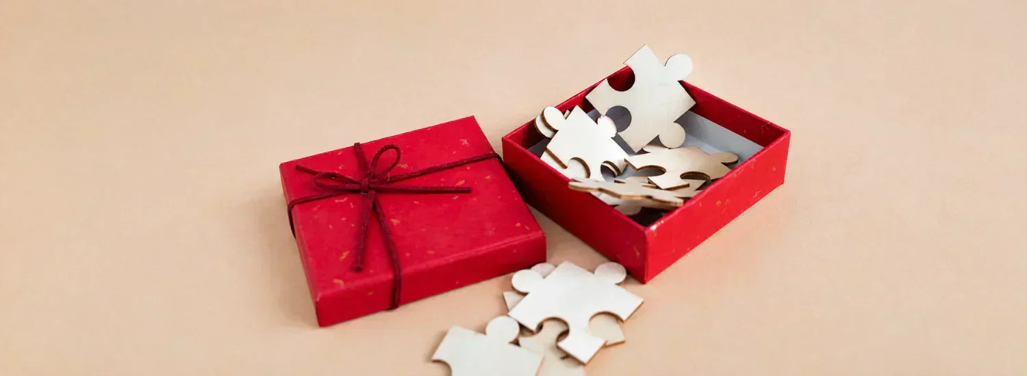 A small red present box, opened to reveal a handful of blank puzzle pieces inside.