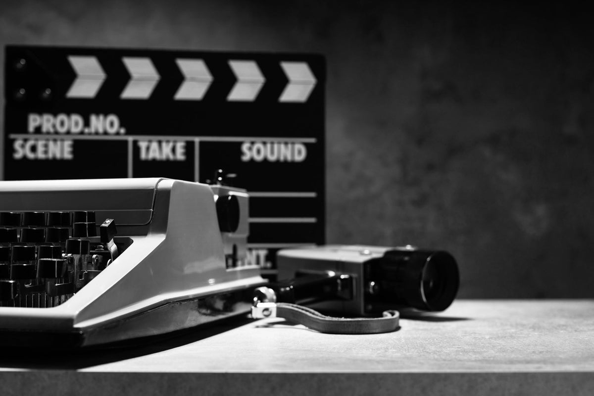 A black-and-white image of a screenwriter keyboard, a vintage camera, and clapper board on a table.