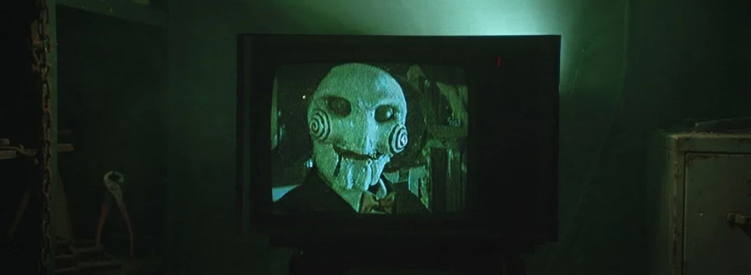 The “I Want to Play a Game” scene from the movie Jigsaw, showing the Jigsaw killer’s puppet on a grainy television screen in a dark room.