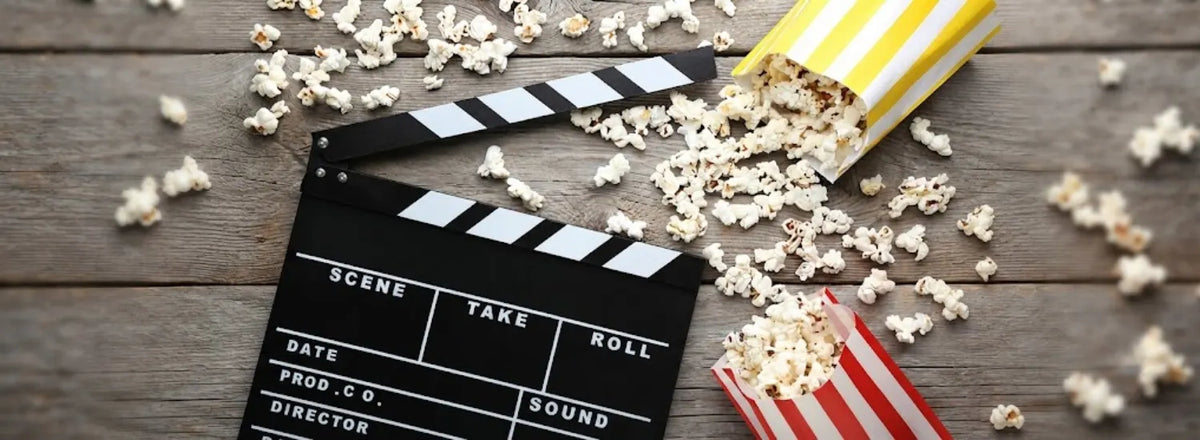 A movie clapper board on a table next to several spilled buckets of popcorn.