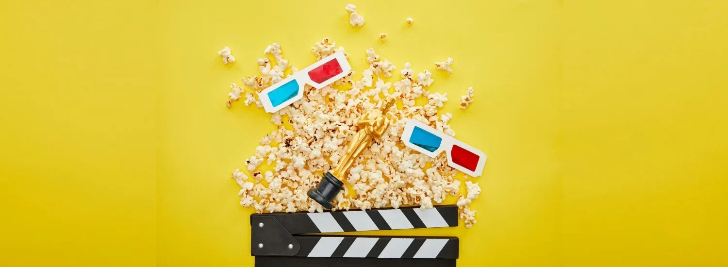 A photo of a golden Oscar statue on a yellow table, surrounded by popcorn, 3d glasses, and a clapper board.