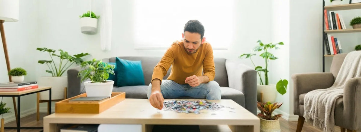 An adult in a well-lit room working on a jigsaw puzzle on a table.
